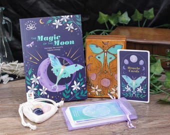 Puede incluir: Un juego de cartas de oráculo de la luna con una caja de madera, un libro titulado "The Magic of the Moon" y una pequeña bolsa con cristales. Las cartas presentan un diseño de polilla azul y púrpura con una luna creciente.