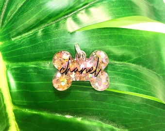 May include: Pink glitter bone-shaped dog tag with the word "chanel" written in black.