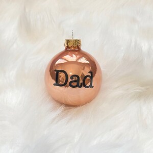 May include: A copper-coloured Christmas bauble with the word "Dad" printed in black lettering.