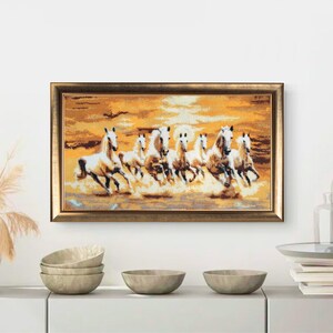 Könnte beinhalten: Ein gerahmtes Kunstwerk, das eine Herde weißer Pferde zeigt, die durch eine goldene Landschaft galoppieren. Die Pferde sind der Mittelpunkt, mit einer detaillierten Darstellung ihrer Formen. Das Kunstwerk befindet sich in einem goldfarbenen Rahmen, was seinen dekorativen Reiz verstärkt.