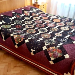 May include: A handmade quilt with a floral pattern and a dark burgundy background. The quilt features a repeating pattern of floral medallions and white and black squares. The quilt is spread over a bed, showcasing its intricate design and craftsmanship.