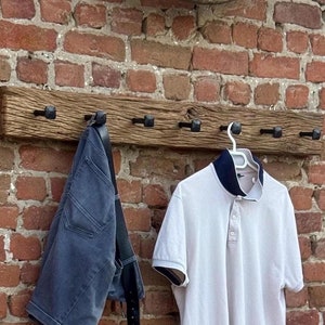 May include: A rustic wooden coat rack with six black metal hooks. A white polo shirt and a pair of blue jeans are hanging on the hooks.