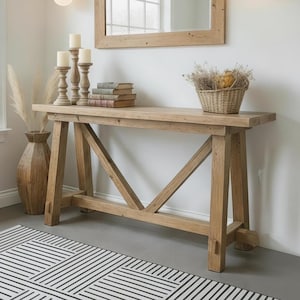 May include: A wooden console table with a rectangular mirror, candles, and a woven basket. The table has a natural wood finish and a geometric base. Two black sconces with globe lights flank the mirror. A black and white patterned rug is on the floor.