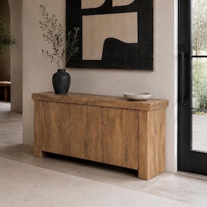 Könnte beinhalten: Ein rechteckiges Sideboard aus Holz mit vier vertikalen Schranktüren in natürlicher Maserung. Darauf steht eine mattschwarze Vase mit grünen Zweigen sowie eine flache, gesprenkelte Steinschale. Darüber hängt ein großes abstraktes Kunstwerk in Schwarz und Beige.