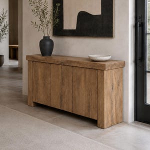 Peut inclure: Une console rectangulaire en bois avec une finition &agrave; grain naturel et quatre portes de placard. Sur le dessus se trouvent un vase noir mat contenant des branches feuillues vertes et un bol peu profond blanc cass&eacute; mouchet&eacute;.