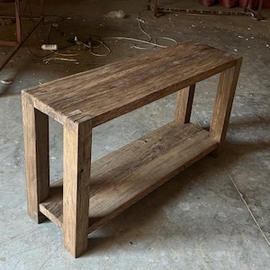 K&ouml;nnte beinhalten: Ein rustikaler Holz-Konsolentisch mit einem einzigen Regal. Der Tisch ist aus recyceltem Holz gefertigt und hat eine nat&uuml;rliche, verwitterte Oberfl&auml;che. Der Tisch ist etwa 122 cm lang und 46 cm breit.
