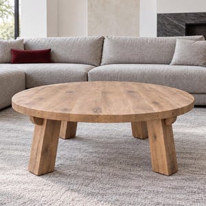 Può includere: Un tavolino rotondo realizzato in legno marrone chiaro con venature visibili, caratterizzato da un piano circolare spesso sostenuto da quattro gambe robuste e angolate che si estendono verso l'esterno per fornire una base stabile.