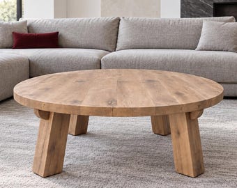 May include: A round coffee table crafted from light brown wood with a visible grain pattern, featuring a thick circular top supported by four sturdy, angled legs that extend outward from the center to provide a stable base for the furniture.