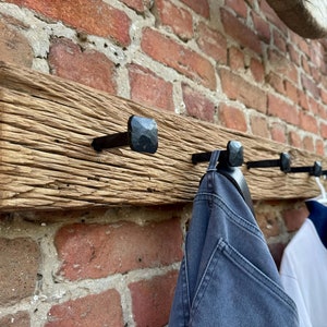 May include: A rustic wooden coat rack with five black metal hooks. The rack is mounted on a brick wall and has a distressed, weathered look.
