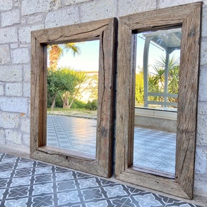 Puede incluir: Dos espejos rectangulares con marco de madera r&uacute;stica. Los espejos est&aacute;n colgados en una pared de piedra y reflejan una vista de un patio con plantas y un suelo de baldosas.