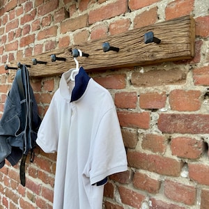 May include: A rustic wooden coat rack with six black metal hooks. The rack is mounted on a brick wall and has a weathered, distressed look.