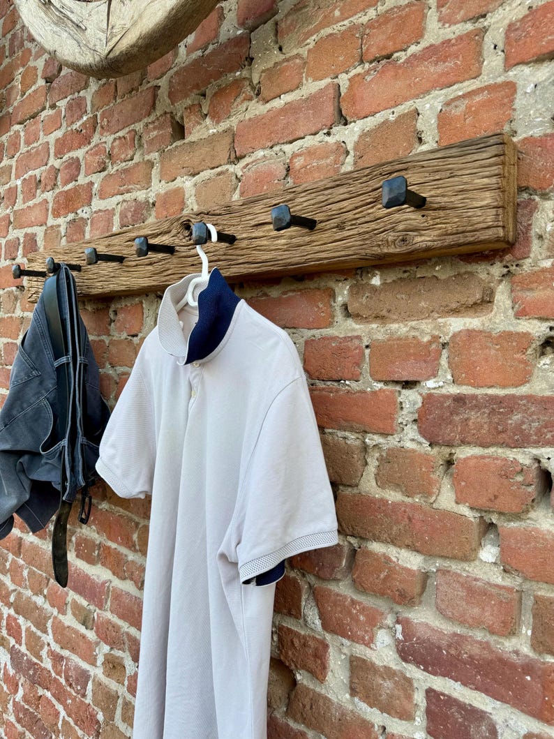 May include: A rustic wooden coat rack with six black metal hooks. The rack is mounted on a brick wall and has a weathered, distressed look.