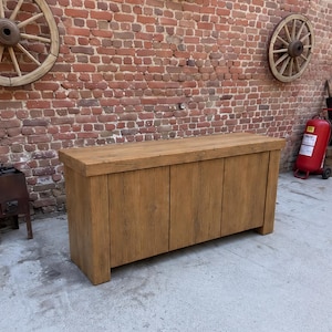 Peut inclure: Un buffet rectangulaire en bois avec une finition brun clair naturelle et des motifs de grain de bois visibles. Ce meuble pr&eacute;sente une surface sup&eacute;rieure &eacute;paisse et trois portes de placard verticales au design plat et lisse.
