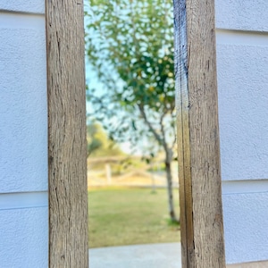 Puede incluir: Un espejo de madera r&uacute;stico con un marco rectangular. El marco est&aacute; hecho de madera recuperada con un acabado natural. El espejo refleja una vista de un c&eacute;sped verde y &aacute;rboles.