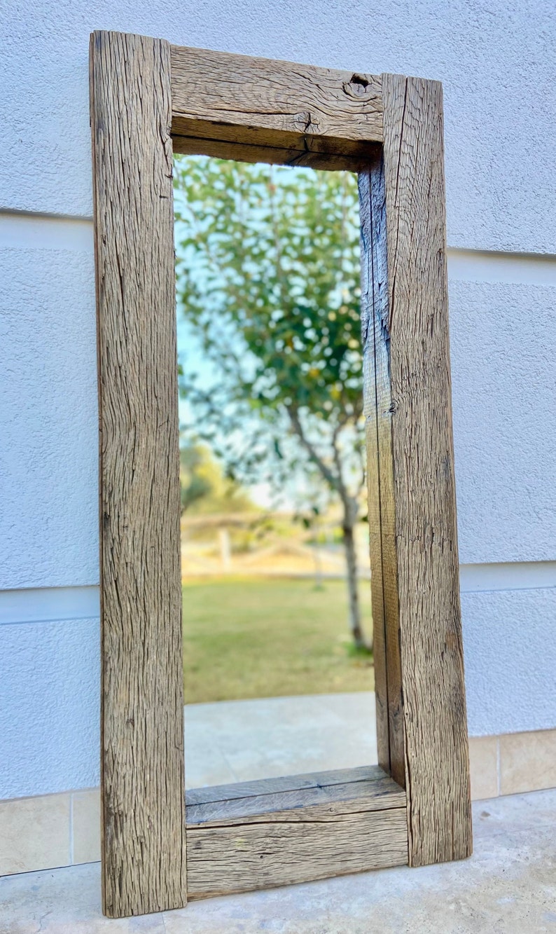 Puede incluir: Un espejo de madera r&uacute;stico con un marco rectangular. El marco est&aacute; hecho de madera recuperada con un acabado natural. El espejo refleja una vista de un c&eacute;sped verde y &aacute;rboles.