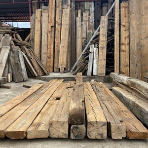 May include: A collection of reclaimed wood beams, stacked and ready for use in a construction project. The beams are rough-hewn and have a natural, rustic look.