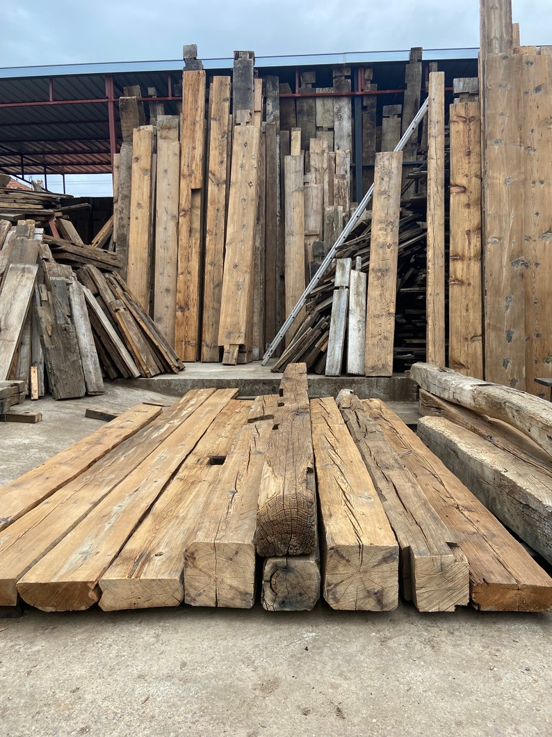May include: A collection of reclaimed wood beams, stacked and ready for use in a construction project. The beams are rough-hewn and have a natural, rustic look.