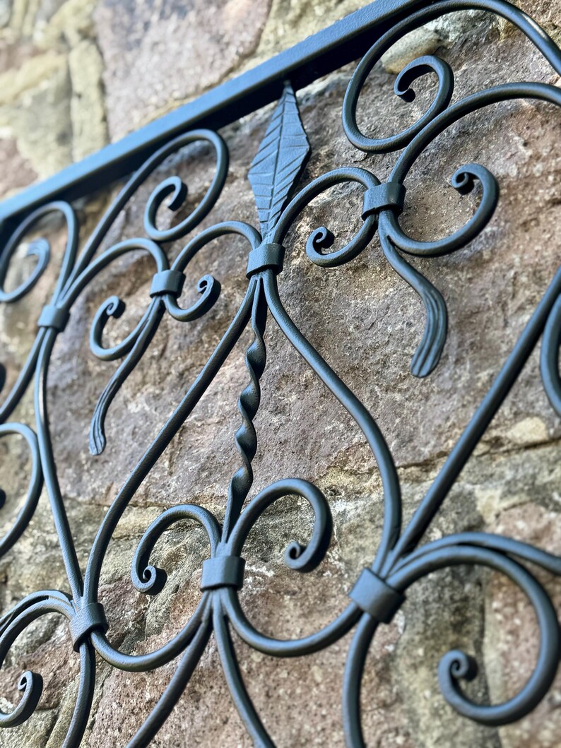 Puede incluir: Decoraci&oacute;n de pared de metal negro con un dise&ntilde;o enrollado. El dise&ntilde;o presenta un motivo central de hoja y espirales intrincados.
