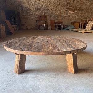 May include: A round wooden coffee table with a rustic, weathered finish. The table has a thick, solid top and four sturdy legs.