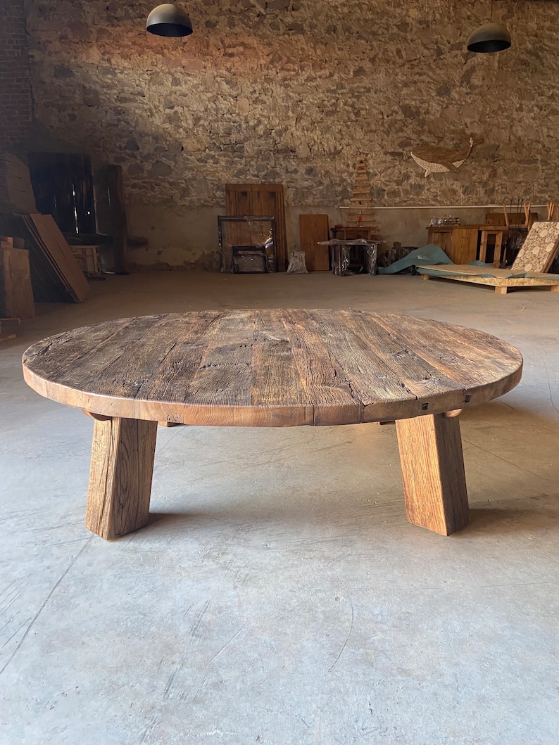 May include: A round wooden coffee table with a rustic, weathered finish. The table has a thick, solid top and four sturdy legs.