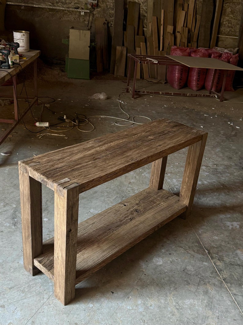 K&ouml;nnte beinhalten: Ein rustikaler Holz-Konsolentisch mit einem einzigen Regal. Der Tisch ist aus recyceltem Holz gefertigt und hat eine nat&uuml;rliche, verwitterte Oberfl&auml;che. Der Tisch ist etwa 122 cm lang und 46 cm breit.