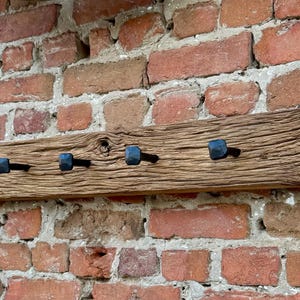 May include: A rustic wooden coat rack with eight black metal hooks. The rack is mounted on a brick wall.