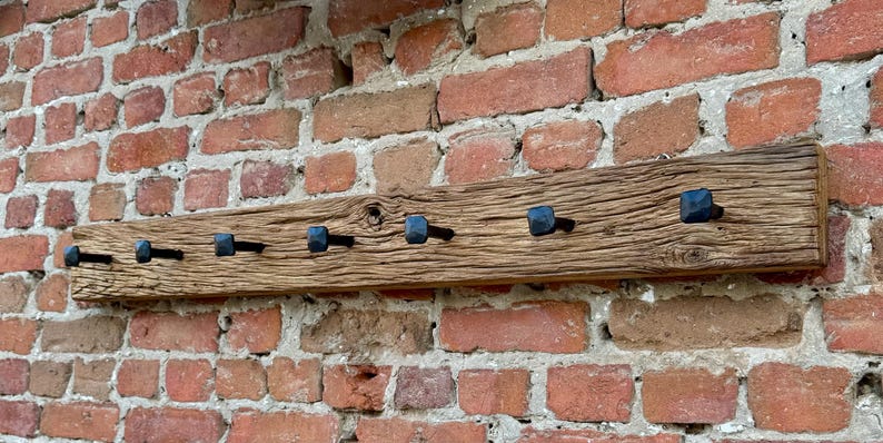May include: A rustic wooden coat rack with eight black metal hooks. The rack is mounted on a brick wall.