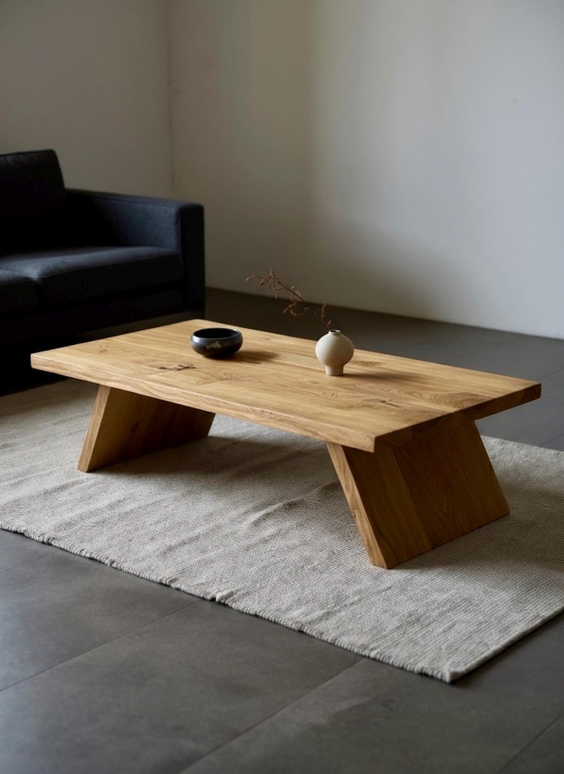 Puede incluir: Mesa de centro rectangular de madera clara con patas anguladas. Un peque&ntilde;o cuenco negro y un jarr&oacute;n blanco con una ramita de flores secas est&aacute;n sobre la mesa. La mesa descansa sobre una alfombra gris claro.