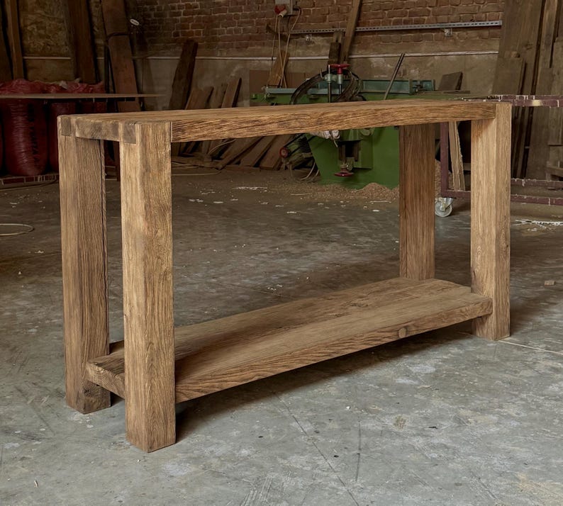 Peut inclure: Une console en bois fabriqu&eacute;e &agrave; la main avec une finition naturelle. La table pr&eacute;sente un plateau rectangulaire et une &eacute;tag&egrave;re inf&eacute;rieure, soutenus par quatre pieds robustes. Le grain du bois est visible, mettant en valeur la beaut&eacute; naturelle du mat&eacute;riau. La table mesure environ 122 cm de long.