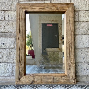 Puede incluir: Un espejo con marco de madera r&uacute;stico con un acabado marr&oacute;n desgastado. El espejo refleja un pasillo con una puerta gris etiquetada como "MIDWAY".