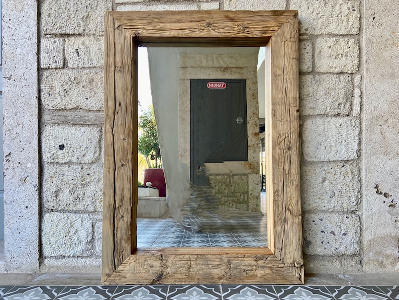 Puede incluir: Un espejo con marco de madera r&uacute;stico con un acabado marr&oacute;n desgastado. El espejo refleja un pasillo con una puerta gris etiquetada como "MIDWAY".