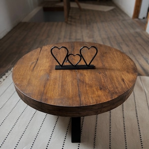 K&ouml;nnte beinhalten: Ein runder Holz-Couchtisch mit dunkelbrauner Oberfl&auml;che und einem schwarzen Metallgestell. Drei metallene herzf&ouml;rmige Skulpturen sind auf der Tischplatte angeordnet.