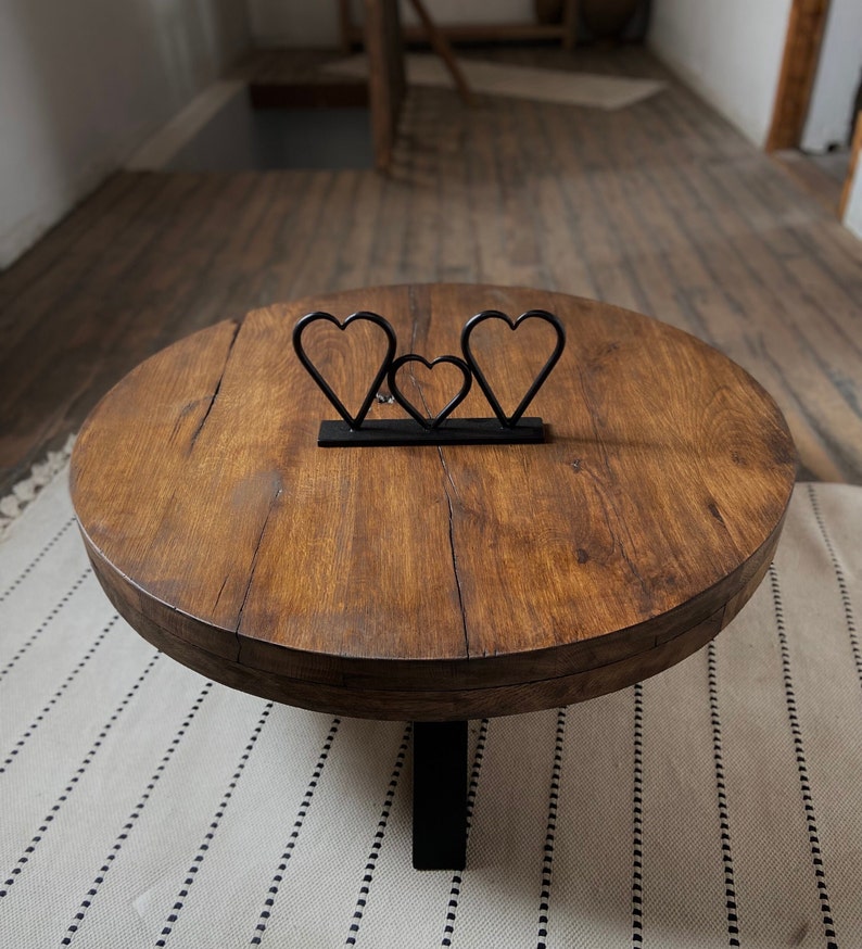 K&ouml;nnte beinhalten: Ein runder Holz-Couchtisch mit dunkelbrauner Oberfl&auml;che und einem schwarzen Metallgestell. Drei metallene herzf&ouml;rmige Skulpturen sind auf der Tischplatte angeordnet.