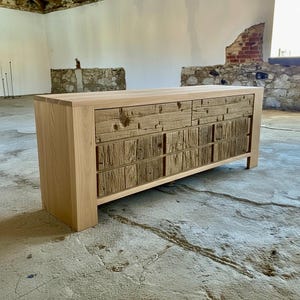 May include: A light-colored wooden dresser with a natural finish. The drawers have a rustic, textured appearance, contrasting with the smooth top and sides. The dresser has a rectangular shape and is set against a neutral background.