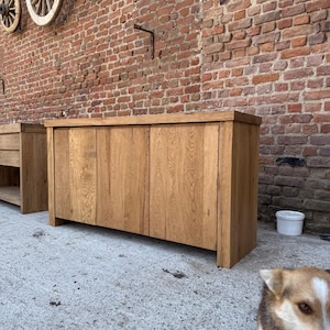 Peut inclure: Un buffet rectangulaire en bois pr&eacute;sentant une finition naturelle en grain de bois brun clair, deux portes d'armoire verticales et une surface sup&eacute;rieure plate. Le meuble est construit avec des panneaux de bois massif &eacute;pais et repose au sol.