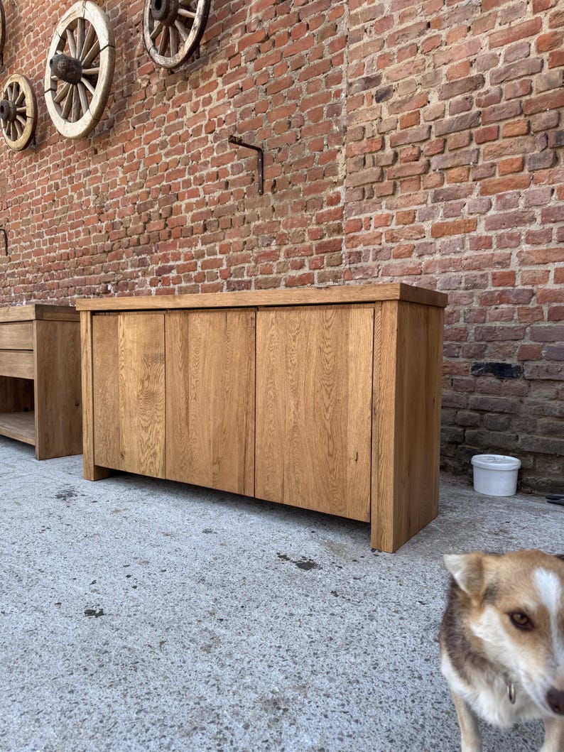 Peut inclure: Un buffet rectangulaire en bois pr&eacute;sentant une finition naturelle en grain de bois brun clair, deux portes d'armoire verticales et une surface sup&eacute;rieure plate. Le meuble est construit avec des panneaux de bois massif &eacute;pais et repose au sol.
