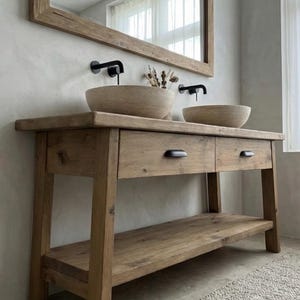 May include: A rustic wooden bathroom vanity with two integrated bowl sinks and black faucets. The vanity features two drawers and a lower shelf, all made of light brown wood. A large wooden-framed mirror hangs above the vanity.