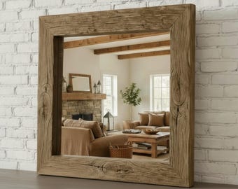 May include: Square mirror with a wooden frame, showcasing a distressed, aged look. The frame is crafted from light brown wood, displaying natural grain and knots. The mirror reflects a living room with a fireplace, sofa, and coffee table, creating a cosy atmosphere.