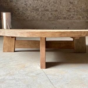 Pu&ograve; includere: Un tavolino da caff&egrave; rotondo in legno con finitura naturale e design semplice e moderno. Il tavolino ha quattro gambe leggermente inclinate e un piano largo e piatto.
