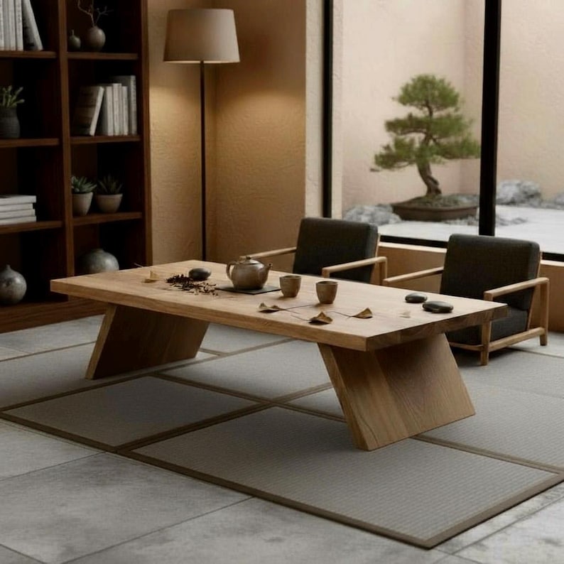 Puede incluir: Una mesa baja de madera clara con patas anguladas, situada en una habitaci&oacute;n minimalista. La mesa est&aacute; puesta con una tetera, tazas y accesorios para el t&eacute;. Dos sillones oscuros est&aacute;n colocados cerca, y un bons&aacute;i es visible a trav&eacute;s de una gran ventana.
