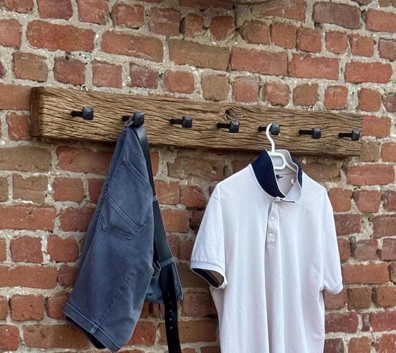 May include: A rustic wooden coat rack with six black metal hooks. A white polo shirt and a pair of blue jeans are hanging on the hooks.