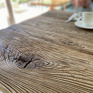 May include: Close-up of a rustic wooden table top with a knot in the wood. The wood has a natural, weathered finish.