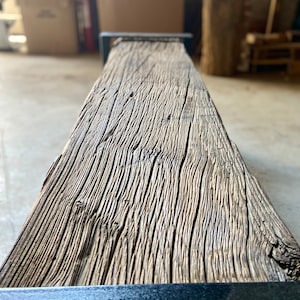 May include: A close-up of a rustic wooden bench with a black metal frame. The wood has a natural, weathered finish and shows the grain of the wood.