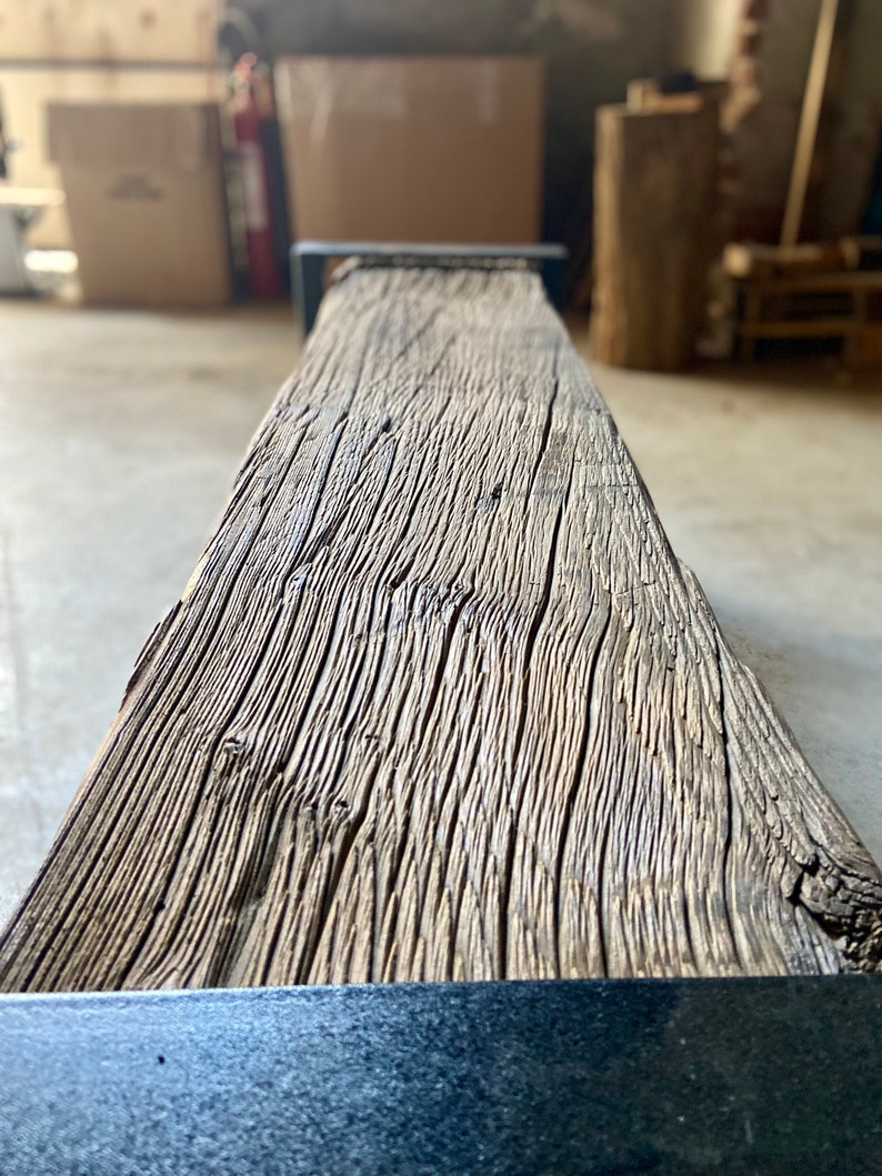 May include: A close-up of a rustic wooden bench with a black metal frame. The wood has a natural, weathered finish and shows the grain of the wood.