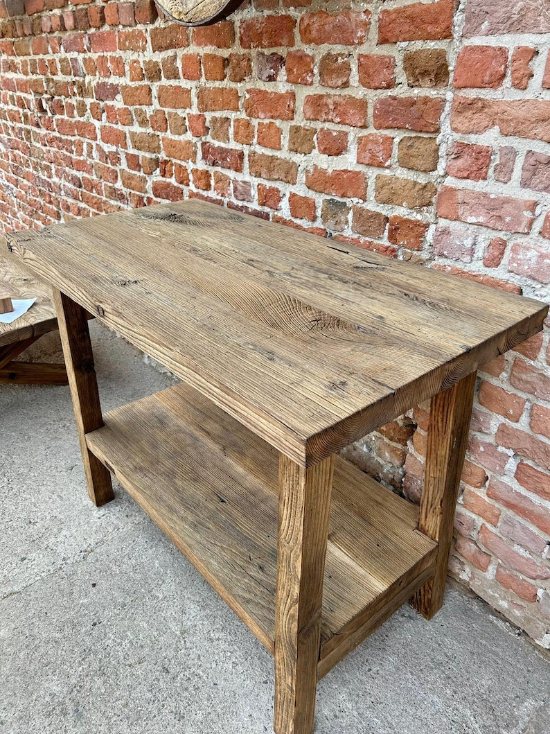 May include: A rustic wooden table with a shelf. The table is made of reclaimed wood and has a natural finish. It is perfect for a farmhouse or industrial style home.
