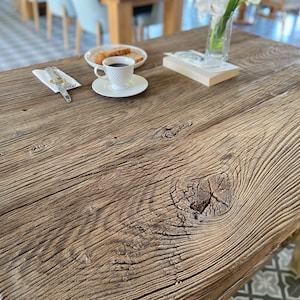 May include: A close-up of a rustic wooden table top with a knot in the wood. The table is made of reclaimed wood and has a natural, weathered finish.