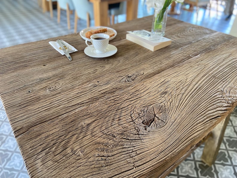 May include: A close-up of a rustic wooden table top with a knot in the wood. The table is made of reclaimed wood and has a natural, weathered finish.
