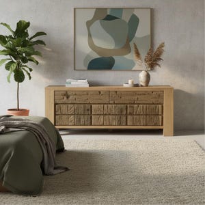 May include: A light oak wood dresser with a textured front, featuring two sets of drawers. Above the dresser is a framed abstract painting with neutral colors. A potted plant and a vase with dried flowers are also visible, creating a warm, inviting interior design.