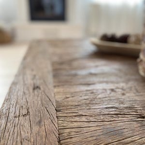 May include: Close-up of a weathered, rustic wooden table. The wood has a natural, aged appearance with visible grain and cracks. The table's surface is a warm, brown tone, suggesting it's made from reclaimed or distressed wood. The focus is on the texture and detail of the wood.