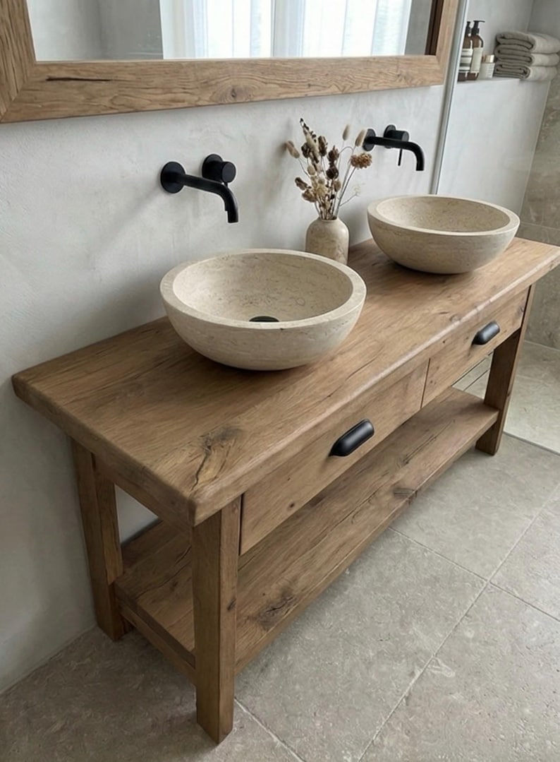 May include: A rustic wooden bathroom vanity with two stone vessel sinks and black faucets. The vanity has two drawers and a lower shelf. A mirror with a wooden frame hangs above the vanity. The overall design is natural and minimalist.